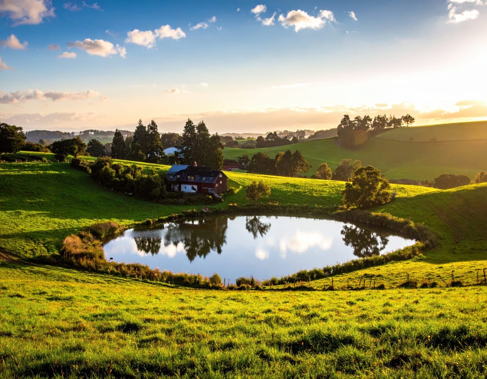Lago natural em gramado com casa e colinas ao fundo